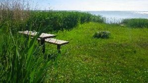 Eine grüne Wiese mit zwei Picknicktischen und einem Gewässer im Hintergrund.