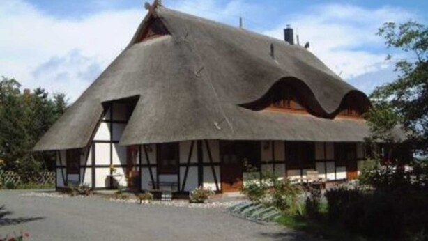 Ein Haus mit einem Strohdach und einem steil ansteigenden Dach sowie einem Schornstein.