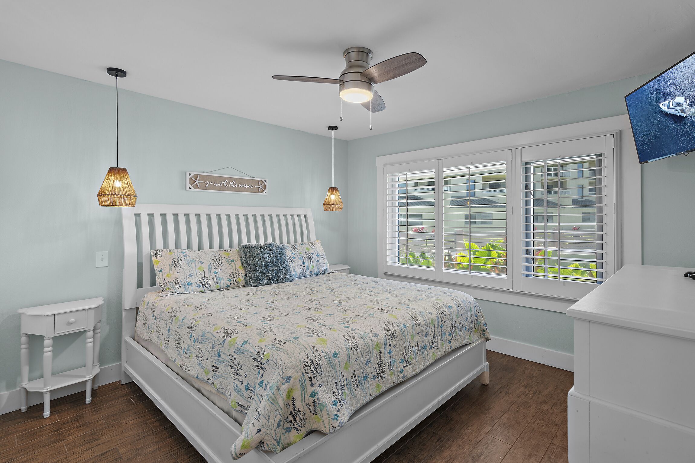 A bedroom with a bed, a ceiling fan, a window with blinds, and a bedside table.
