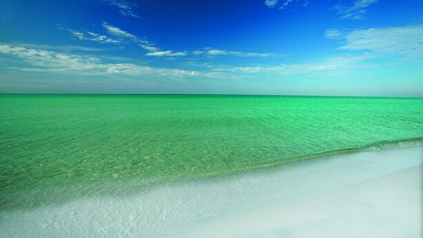 A beach with clear turquoise water and a white sandy shore under a blue sky.