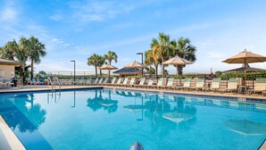 A swimming pool with lounge chairs and umbrellas, surrounded by palm trees.