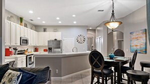 A modern kitchen with white cabinets, a central island, and a dining area with dark chairs. - Experience magic! HR Golf Course view 5bd/3b w/pool-spa near all Disney Parks (Davenport)