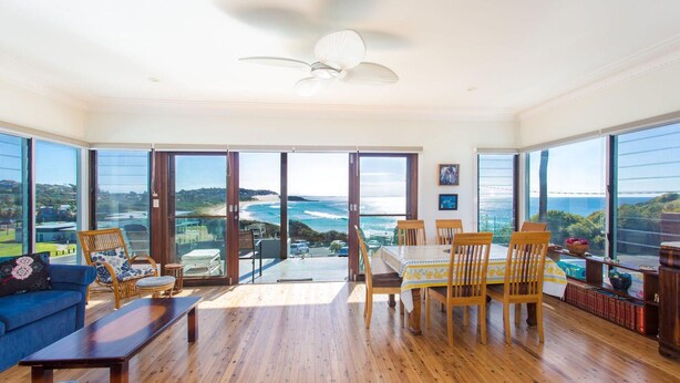 A spacious living room with a large sliding glass door leading to a balcony overlooking a beach. - 18 Cliff Road - Opposite One Mile Beach! (Forster)
