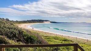 A coastal landscape with a sandy beach, a wooden fence, and a clear sky. - 18 Cliff Road - Opposite One Mile Beach! (Forster)
