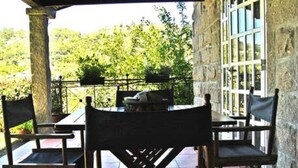 An outdoor patio with a table and chairs, stone walls, and a view of greenery.