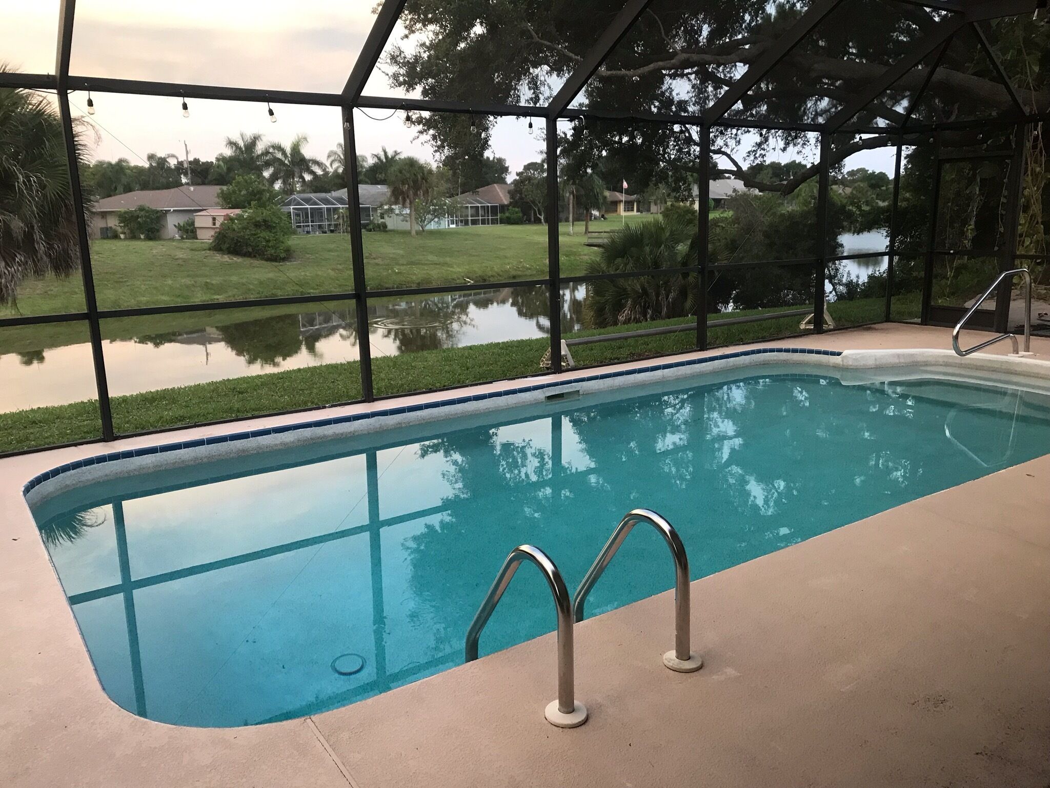 A swimming pool with a clear view of the surrounding area, including a grassy lawn and a body of water.