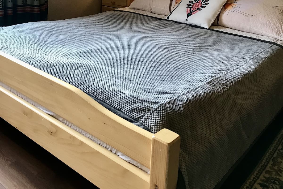 Ein Schlafzimmer mit einem hölzernen Bett, einem Nachttisch mit Lampe, gemusterten Vorhängen und einem Wandbild.