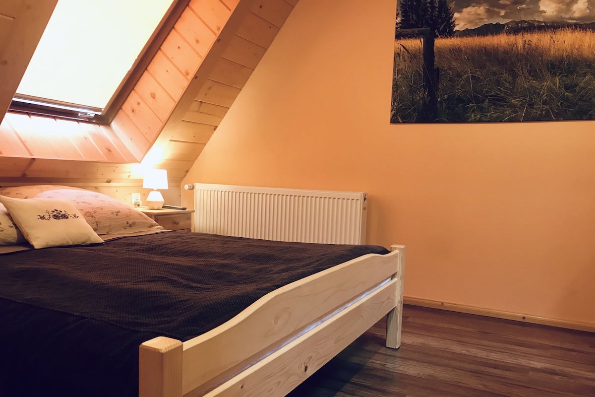 Ein Schlafzimmer mit schrägverdeckter Decke, einem hölzernen Bett, einem weißen Heizkörper und einem Bild an der Wand.