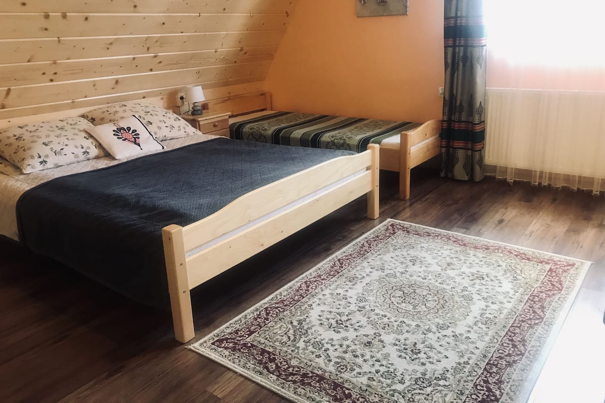 Ein Schlafzimmer mit einem hölzernen Bett, einem kleinen Nachttisch, einem Beistelltisch, einem gemusterten Teppich und einem Bild an der Wand.