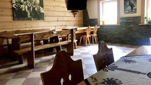 Una habitación rústica con bancos de madera y una mesa, un televisor montado en una pared de piedra y cuadros enmarcados en las paredes.