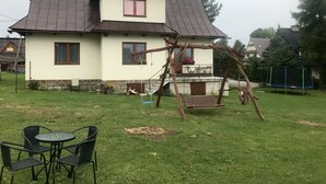 Una casa de dos pisos con techo inclinado, un balcón con mobiliario exterior y un columpio en el jardín.