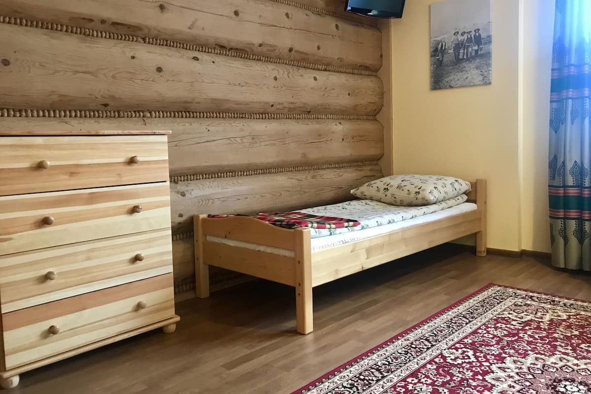 Ein Zimmer mit einem hölzernen Bett, einem Holzschrank, einem an der Wand befestigten Fernseher und einem gemusterten Teppich.