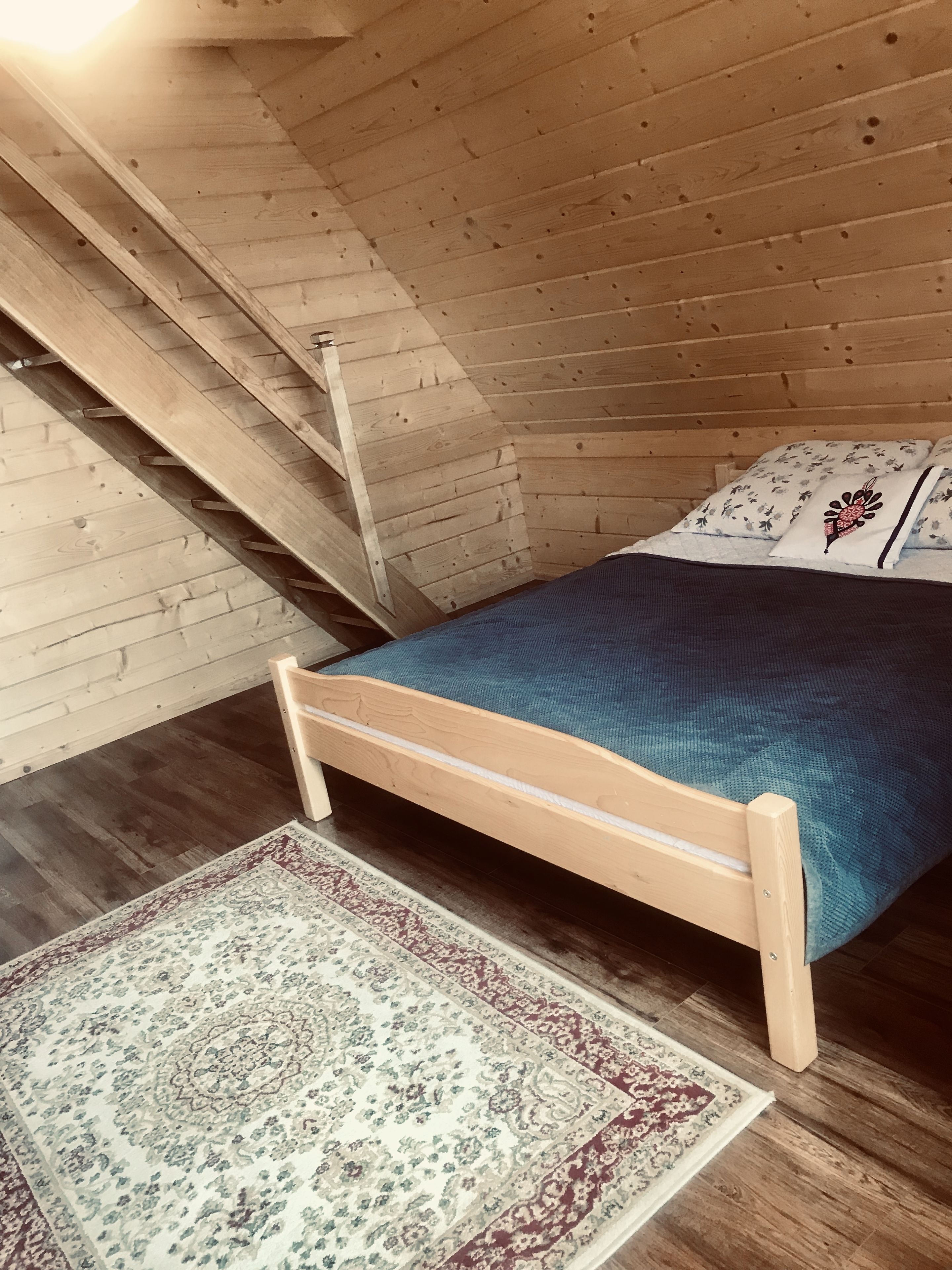 Une chambre à coucher aménagée dans les combles, avec un lit, un tapis à motifs et une échelle en bois.