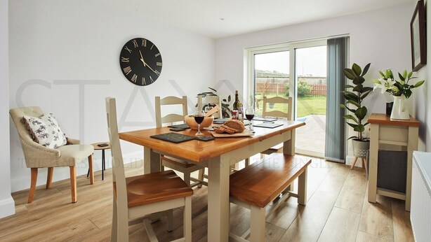 Un comedor con mesa de madera, sillas, un reloj y vistas al exterior.