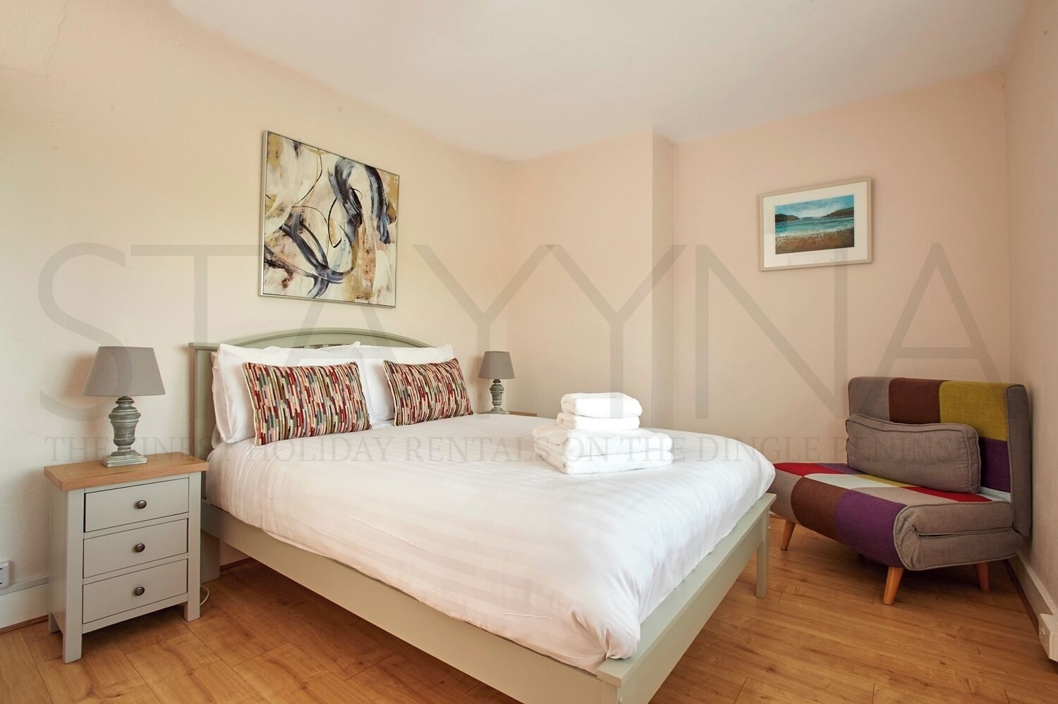 Ein Schlafzimmer mit einem Bett, zwei Nachttischen, einem Sessel und Bildern an den Wänden.