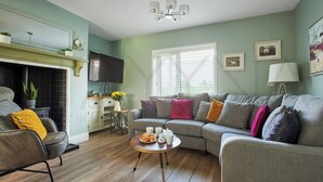 Una sala de estar acogedora con sofá, sillón y mesa de centro. Hay una chimenea, un televisor y una ventana con persianas.