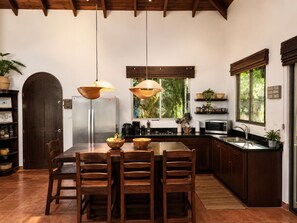 A modern kitchen with a dining table, chairs, pendant lights, and a refrigerator. - Villa Colibrí, 3 BR, walk to beach, private pool (Santa Teresa Beach)