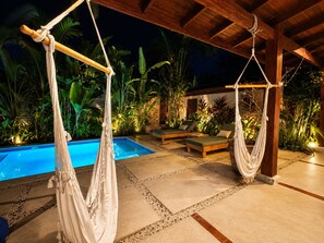 Un área de piscina con dos hamacas, sillas de descanso y un deck con losetas de piedra.