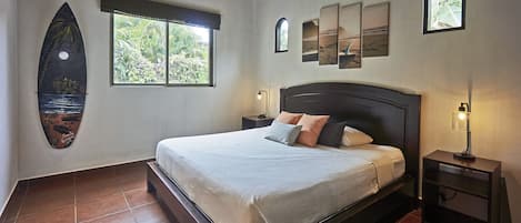 A bedroom with a bed, a nightstand, a window, and a surfboard decoration.