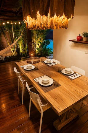 A wooden dining table set for four with white chairs, a hanging light fixture, and a view of a pool. - Villa Colibrí, 3 BR, walk to beach, private pool (Santa Teresa Beach)