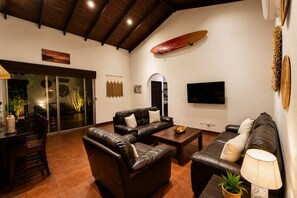 Sala de estar com sofás de couro, mesa de centro, televisão e uma prancha de surf na parede.