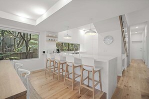 Una cucina moderna con isola centrale, sgabelli da bar, illuminazione a sospensione e un'ampia finestra che si affaccia sul verde.