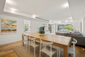 A modern interior with a wooden dining table, white chairs, a grey sofa, and a large window.