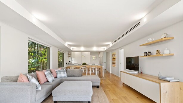 A modern living room with a sofa, ottoman, TV, and wooden flooring. - Audrey - Little Cove (Noosa Heads)