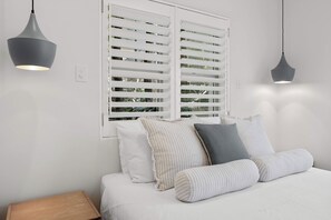 Una camera da letto con un letto, cuscini, un comodino e due lampade a sospensione.