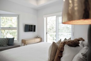 A bedroom with a bed, a bedside table, a TV mounted on the wall, and a window with blinds. - Audrey - Little Cove (Noosa Heads)
