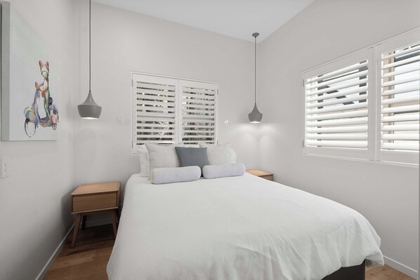 A bedroom with a bed, two bedside tables, a nightstand, a painting, and two pendant lights. - Audrey - Little Cove (Noosa Heads)