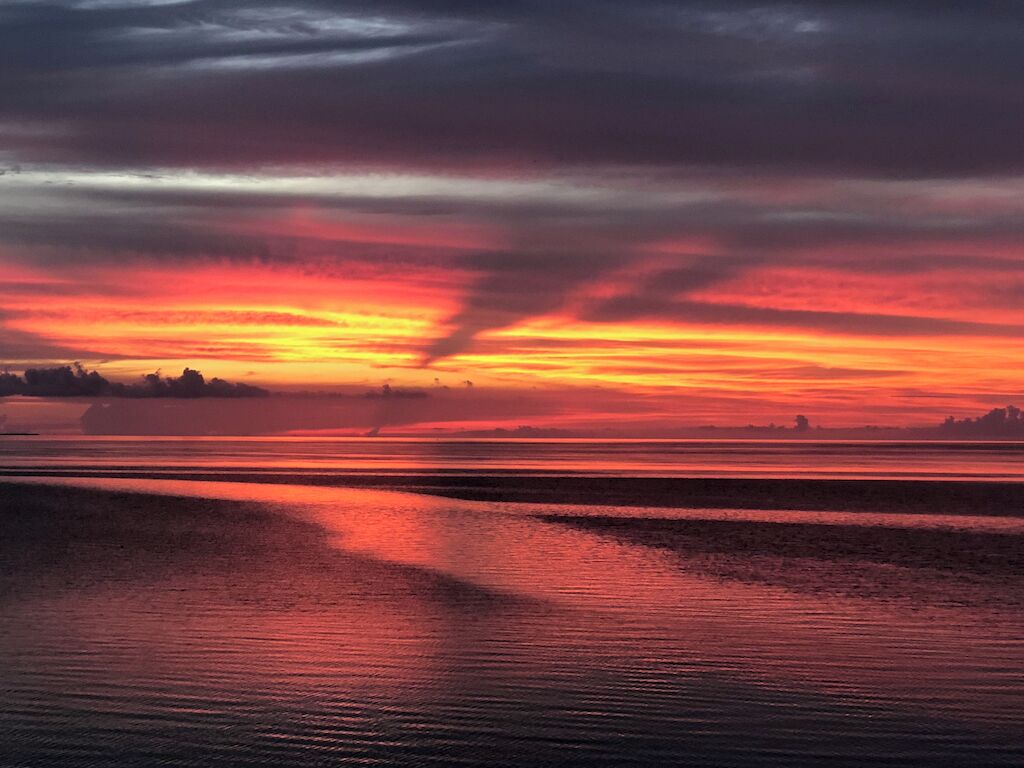 Un coucher de soleil sur une étendue d'eau calme, avec une côte visible au loin.