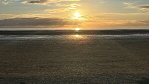 Ranta, jossa aurinko laskee horisontin taa ja muodostaa rantaviivasta tumman siluetin.