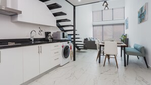 Una cocina moderna con armarios blancos, lavadora integrada y una zona de comedor con mesa y sillas.