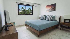 Un dormitorio con cama, televisor, ventana y un cuadro.