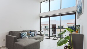 Una sala moderna con un sofá seccional gris, ventanas amplias y plantas en macetas.