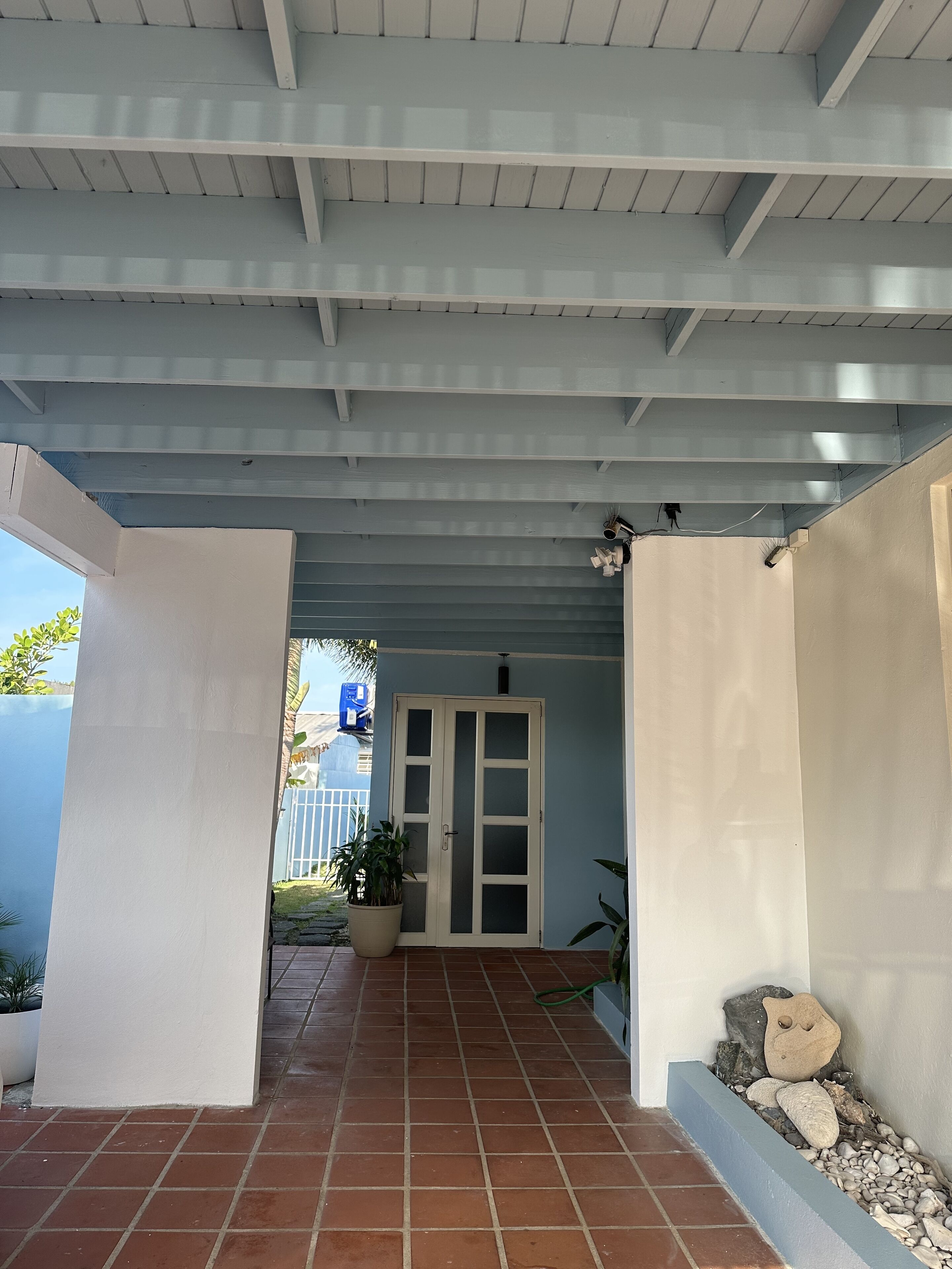 A covered outdoor area with a tiled floor, a door, and a potted plant.