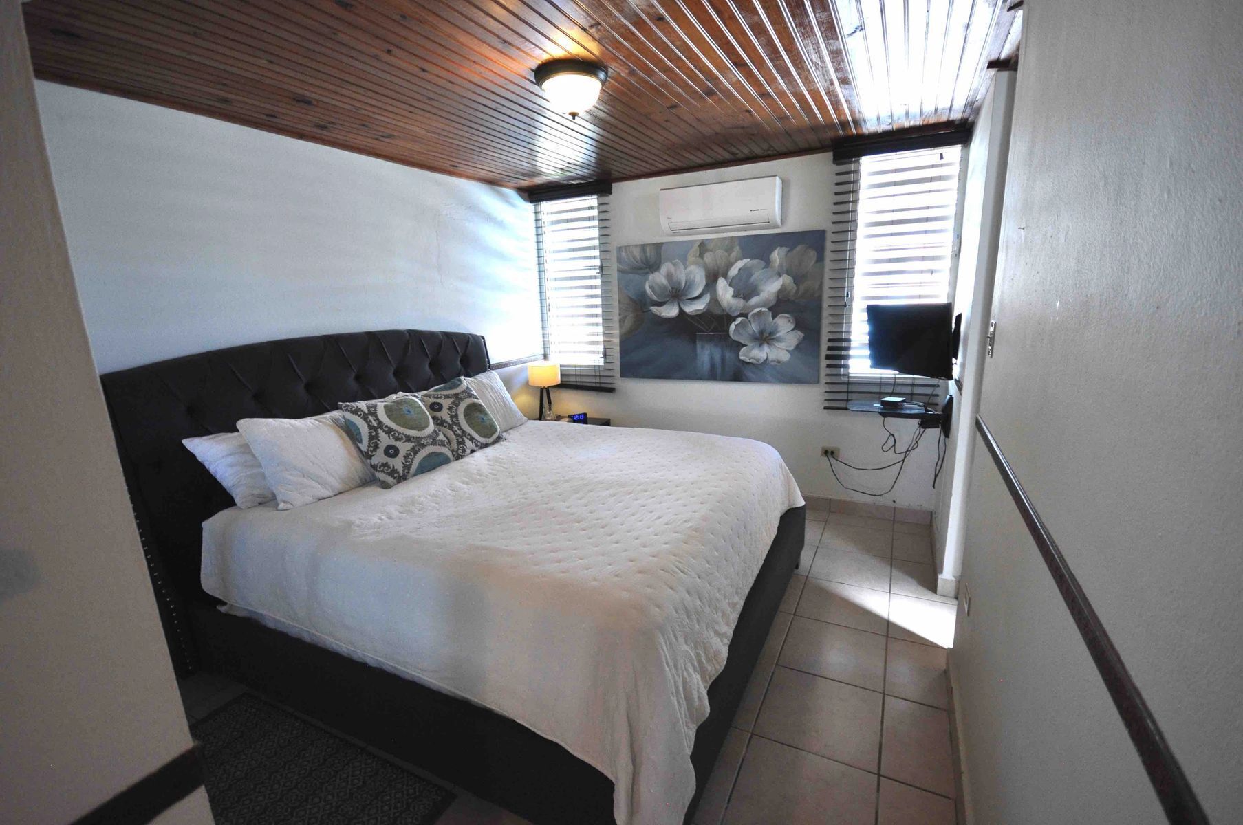 A bedroom with a bed, a wall-mounted air conditioner, and a window with blinds.