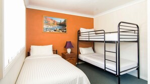 Une chambre avec deux lits, dont un lit simple et un lit superposé, une table de chevet avec une lampe et un tableau au mur.