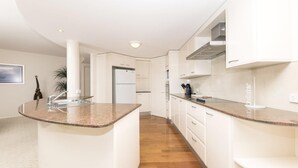 A modern kitchen with white cabinetry, granite countertops, and a stainless steel range hood. - Le Point 101 - Walking distance to Main Beach (Forster)