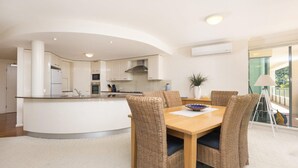 A modern kitchen with white cabinets, a central island, and a dining area with wicker chairs and a wooden table. - Le Point 101 - Walking distance to Main Beach (Forster)