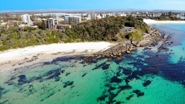 An aerial view of a coastal area with a beach, rocky shoreline, and buildings in the background. - Le Point 101 - Walking distance to Main Beach (Forster)