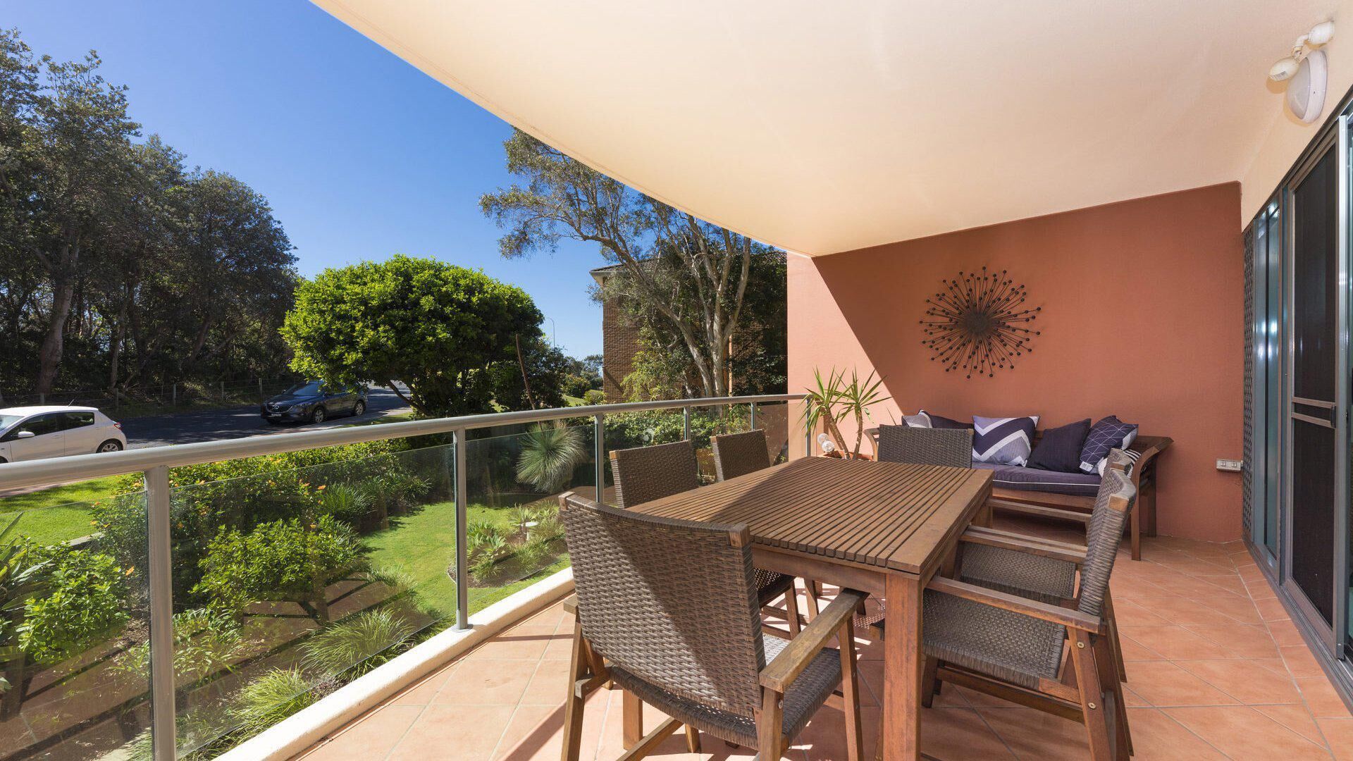 Un balcon avec une table et des chaises en bois, un canapé avec des coussins et un élément décoratif mural.