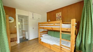 Dormitorio con literas, paredes de madera, un armario blanco y una cortina verde.