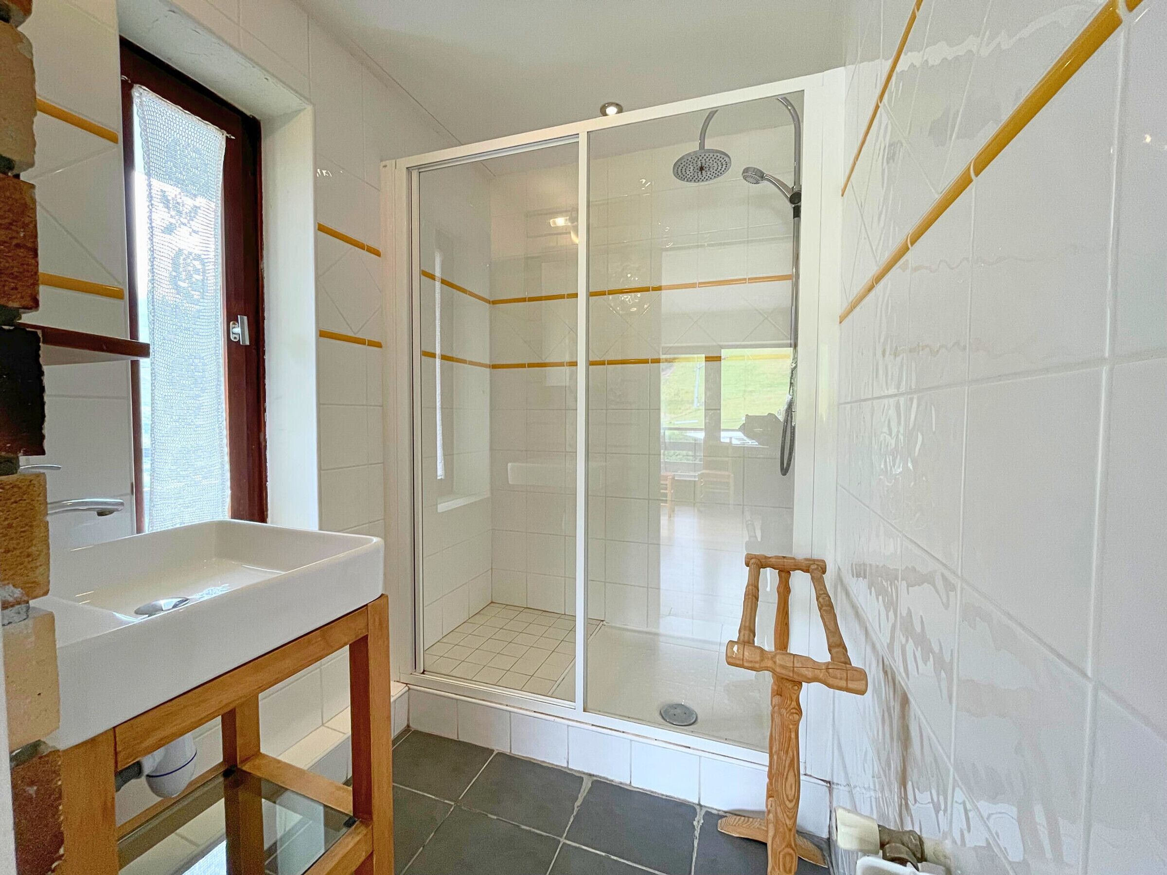 A bathroom with a glass-enclosed shower, a wooden stool, and a sink.