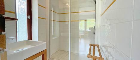 A bathroom with a glass-enclosed shower, a wooden stool, and a sink.