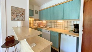 Cocina compacta con gabinetes color turquesa, lavavajillas blanco y cafetera.