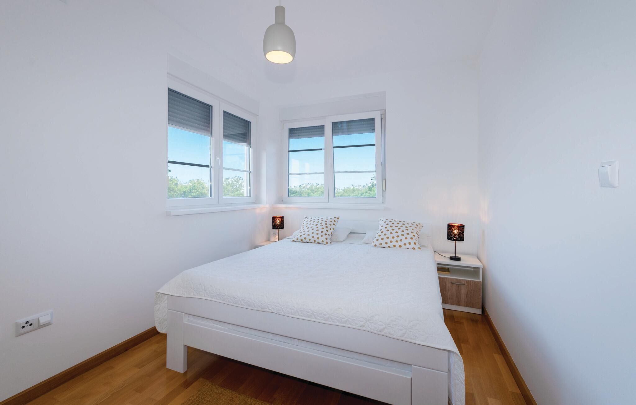 A bedroom with a large bed, two bedside tables with lamps, and two windows.