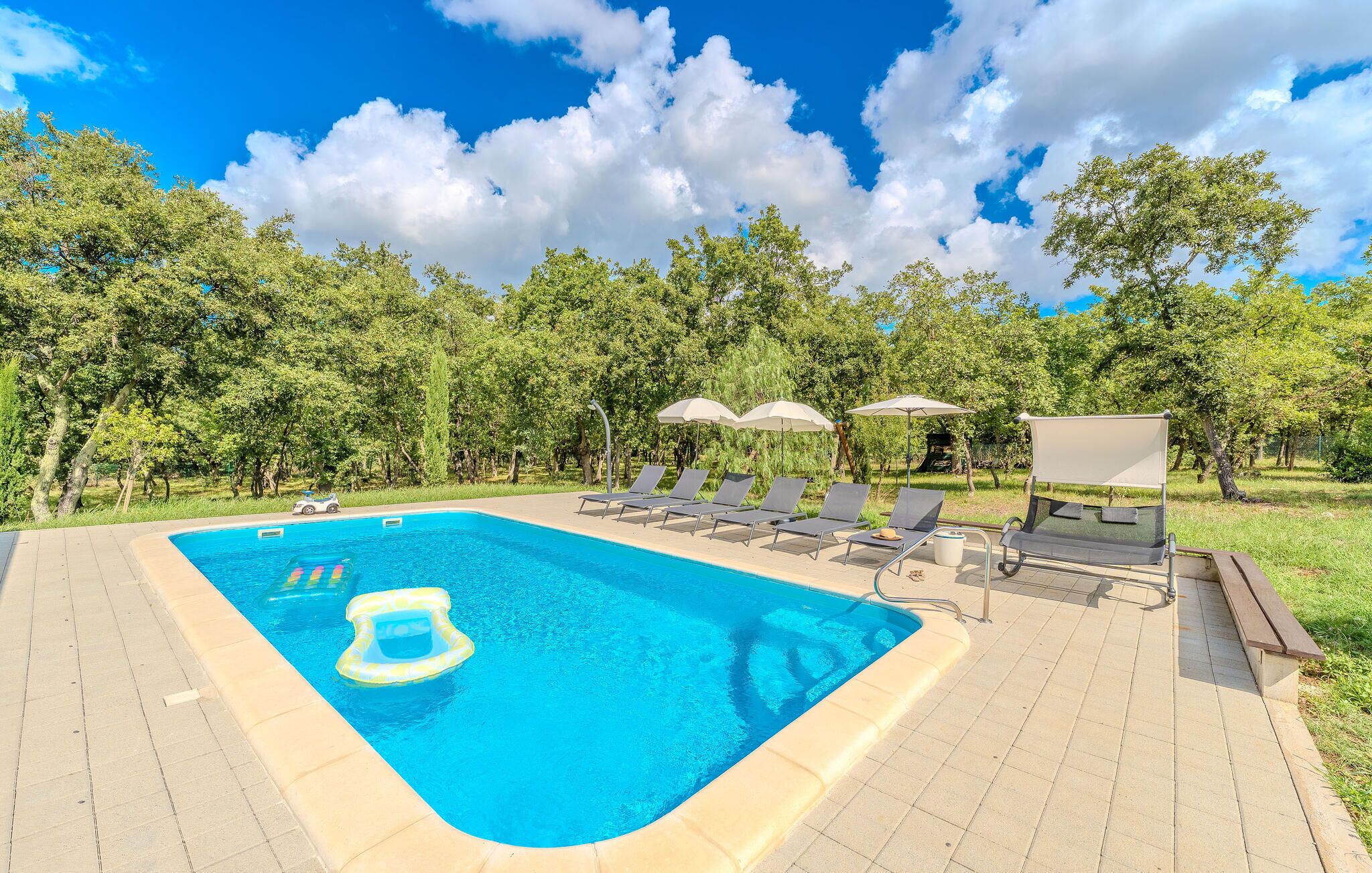 A swimming pool with lounge chairs and umbrellas, surrounded by trees.