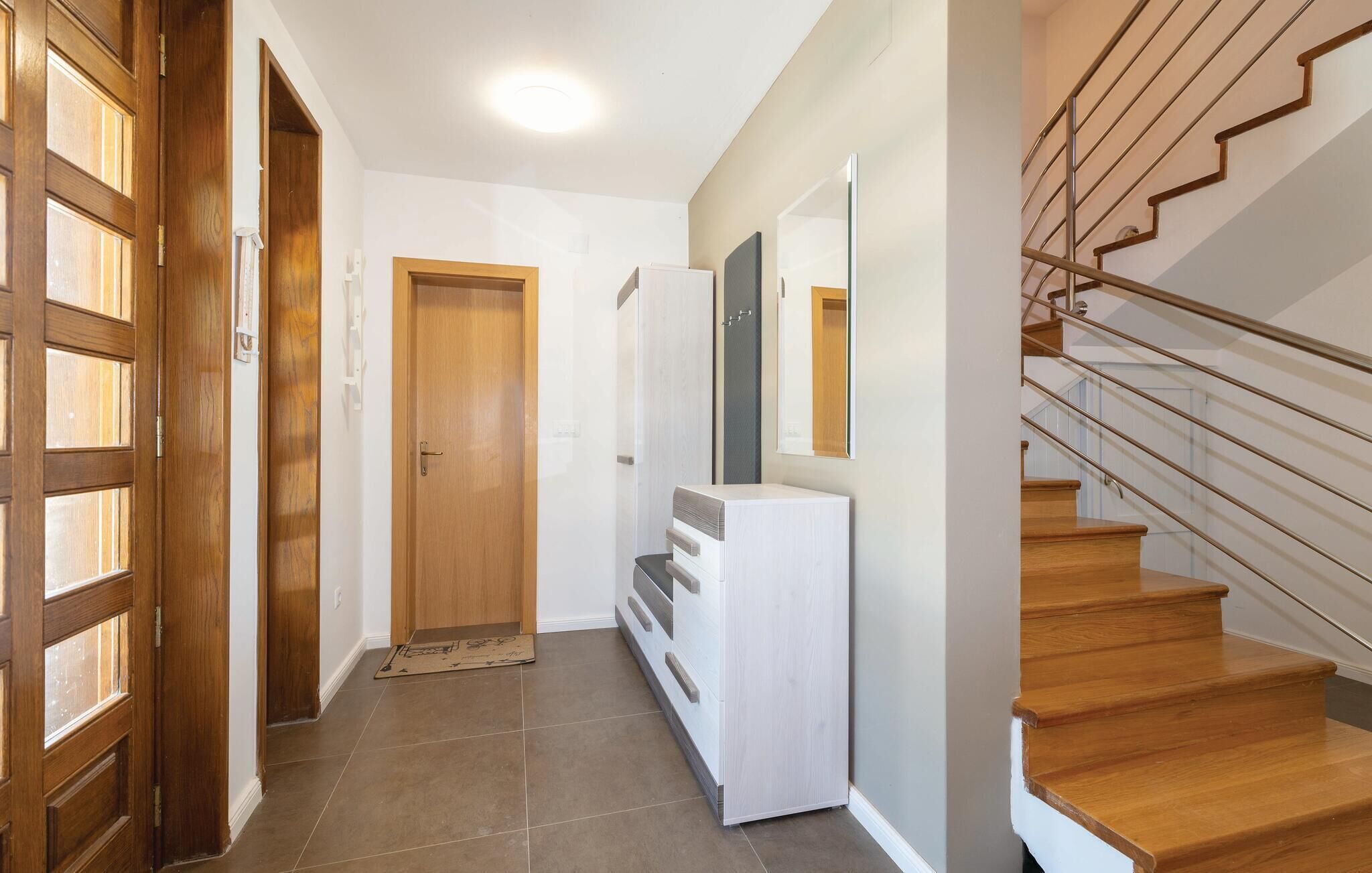 Un pasillo con puertas de madera, una consola blanca y una escalera con barandillas de metal.